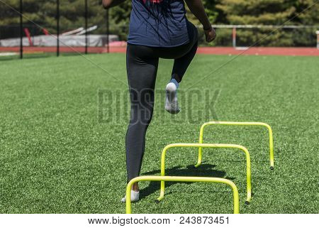 A High School Girl Is Performing Speed And Agility Drills Over Hurdles With No Shoes On, Only Socks 