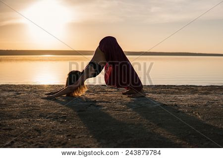 Silhouette Woman On The Beach At Sunset Doing Yoga Asana. Morning Natural Stretch Warm-up Training