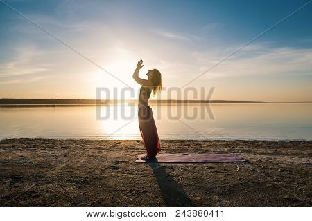 Silhouette Woman On The Beach At Sunset Doing Yoga Asana. Morning Natural Stretch Warm-up Training