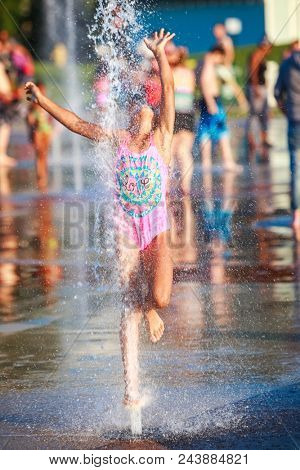 Girl jumping into the fountain at a splash park, shallow focus on water splash