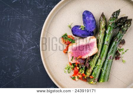 Modern fried tuna fish filet with green asparagus blue potatoes und vegetable chili relish as top view on a plate with copy space left 