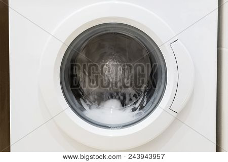 Washing Machine Door With Rotating Garments Inside. Focus In The Center Of Dirty Laundry