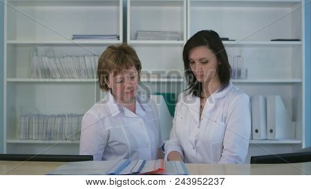 Two Nurses Sorting Out Folders And Files At Hospital Reception
