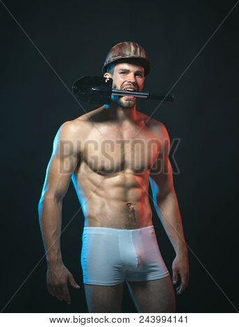 Sexy Worker Concept. Muscle Worker With Nude Torso In Boxer Shorts With Shovel In Teeth. Constructio