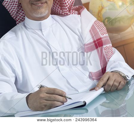 Smiling Senior Saudi Businessman Hand Writing At His Desk