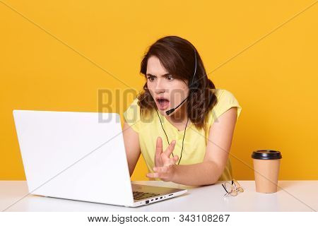 Woman Seatting At Table And Looking At Her Laptop Screen In Consternation And Horror, Keeping Mouth 
