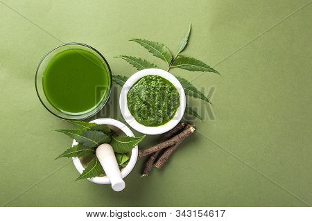 Medicinal Neem Leaves In Mortar And Pestle With Neem Paste, Juice And Twigs On Green Background
