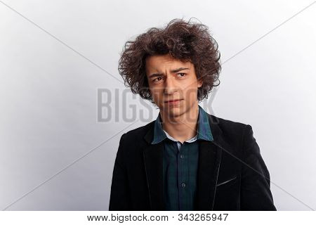 Young Man In Jacket And Shirt, With Wavy Hair, Having A Confused Facial Expression, In Studio, Over 