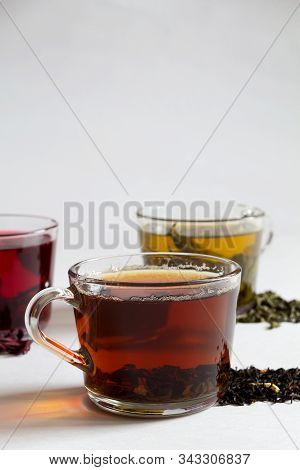 Black Hot Tea With Dry Leaves.three Glass Cups With Black, Red And Green Tea With Dry Leaves On A Wh