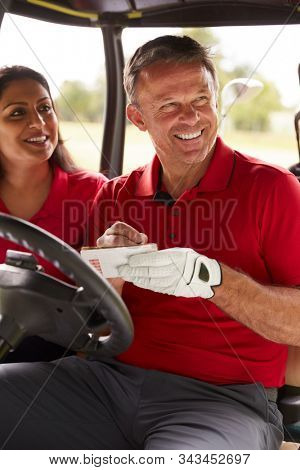 Mature Couple Playing Golf Marking Scorecard In Buggy Driving Along Course