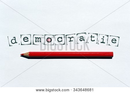 The Dutch Word 'democratie' (democracy) Written With Stamps And Ink On White Paper, And A Red Wooden