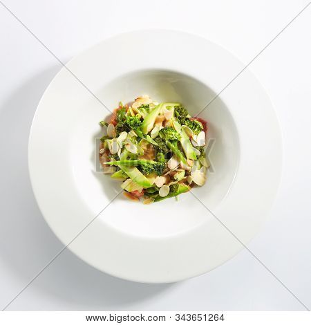 Salad with avocado, broccoli, cucumber, avocado, grapefruit and almonds on white restaurant plate isolated. Top view of gourmet green salat, healthy and tasty dinner