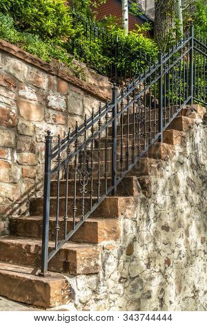Outdoor Staircase With Stone Steps And Black Metal Railing Against A Fence
