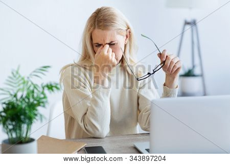 Tired Businesswoman Massaging Nosebridge, Working On Laptop At Workplace