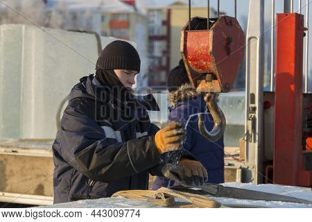 Portrait Of A Worker In A Blue Jacket With A Hood At The Hook Of A Truck Crane