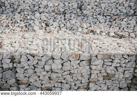 Granite Stones Behind A Metal Grate For Strengthening The Slope. Stones Behind The Wire. Grey Textur