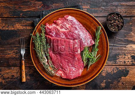 Two Flap Or Flank Raw Beef Steaks On A Rustic Plate With Herbs. Dark Wooden Background. Top View