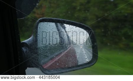 Rain Drops On Rearview Mirror Reflection Of Road. Landscape With Empty Highway Going Through The Gre