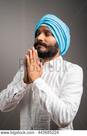 Side View Shot Of Indian Sikh Man Doing Namste Or Praying To God On Gray Background With Closed Eyes