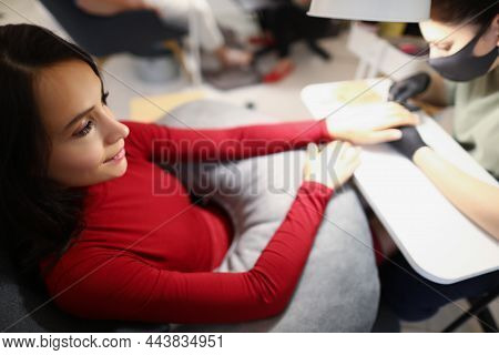 Top View Of Young Female Sitting On Appointment In Beauty Studio And Enjoy Getting Her Nails Done. N