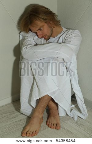 Mentally ill man in strait-jacket in room corner