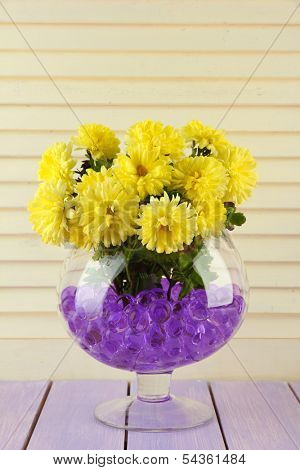 Beautiful flowers in vase with hydrogel on table on wooden background