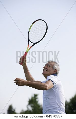 Happy senior man playing tennis, low angle view