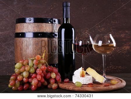 Supper consisting of Camembert cheese, wine and grapes on cutting board and wine barrel on wooden table on brown background