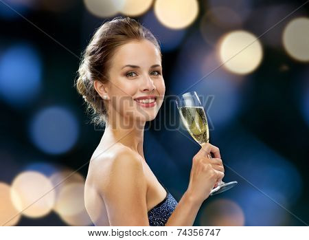 party, drinks, holidays, luxury and celebration concept - smiling woman in evening dress with glass of sparkling wine over night lights background