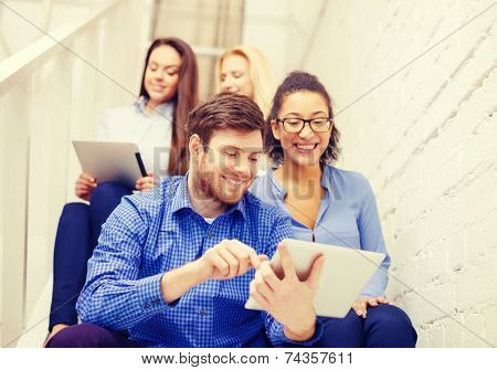 business, technology and startup concept - smiling creative team with tablet pc computer sitting on staircase