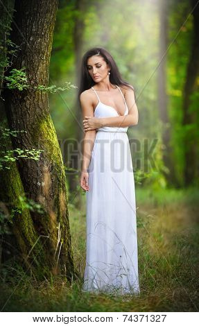 Lovely young lady wearing an elegant long white dress enjoying the beams of celestial light on her