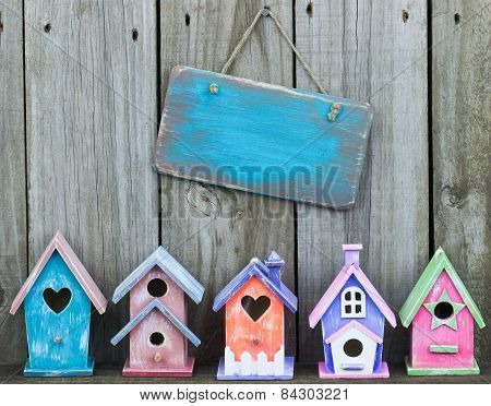 Blank wood sign hanging on fence over colorful birdhouses