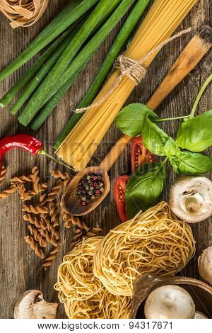 Italian food background with raw pasta and vegetables on wooden table