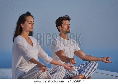 young couple practicing yoga at sunset in modern home terace with ocean and sunset in background