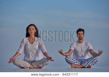 young couple practicing yoga at sunset in modern home terace with ocean and sunset in background