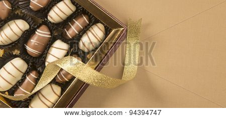 Fine date chocolates in a golden box with loose ribbon wrapped around.