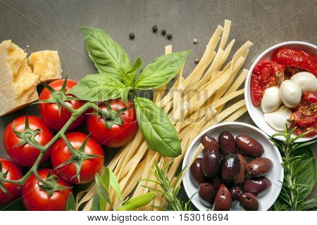Italian food background, over slate.  Top view. Variety of ingredients, including pasta, tomatoes, basil, olives, parmesan, mozzarella, garlic, and herbs.