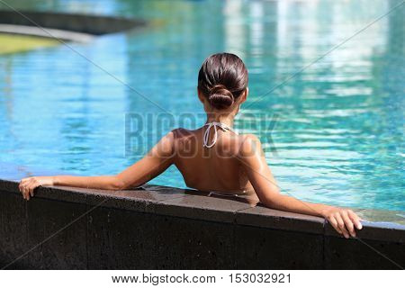Swimming pool spa retreat relaxation. Relaxing woman lying from the back on infinity edge enjoying sun and serenity in summer holiday travel vacation at resort hotel. Unrecognizable people holidays.