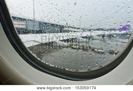 selective focus rain drop from window seat inside airplane with blurred wing background at plane park in airport before taking off