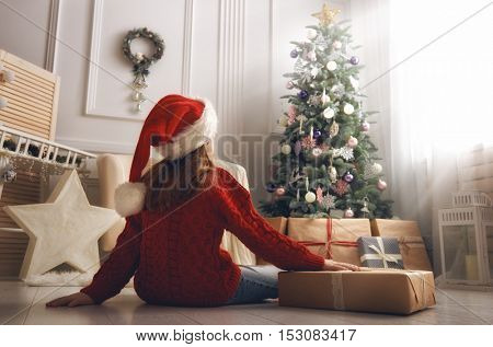 Merry Christmas and Happy Holidays! Cheerful cute little child girl with present. Kid holds a gift box near Christmas tree indoors.