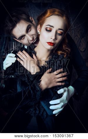 Bloodthirsty male vampire in medieval dress is biting a beautiful lady. Halloween. 