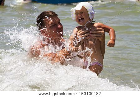 a young father and young daughter swimming in the sea in the waves laugh