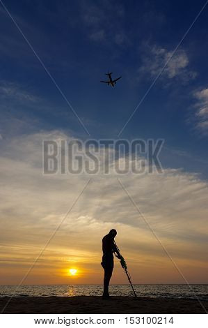 a treasure hunter with Metal detector on sunset on the beach