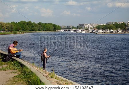 Saint Petersburg Russia - May 21 2014: gitarist and a fishermansitting - standing on the niva river on sunny day