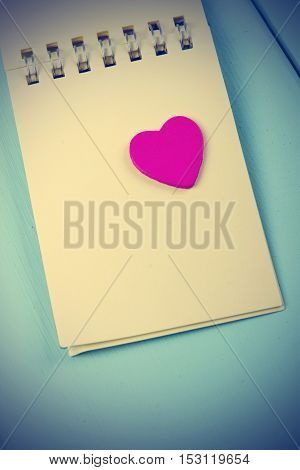 wooden pink heart and a notebook on a spring on a wooden turquoise background. vertical shot. love notes. vintage filter