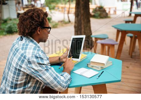Curly arfican young man using blank screen tablet in outdoor cafe