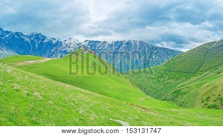 The Tsminda Sameba (Holy Trinity) Church in Gergeti is surrounded by green mountain slopes at the foot of Kazbek Mount Georgia.
