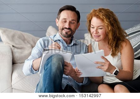 Comparing ideas. Pretty ginger woman leaning to her male partner holding notebook and pencil to get more information.