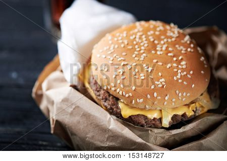 Unhealthy cheeseburger in the paper container with paper napkins on a dark wooden background. Close up