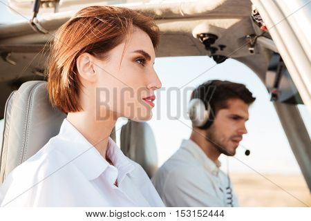 Close up portrait of a young pilot and beautiful stewardess sitting together inside airplane cabin waiting to take off